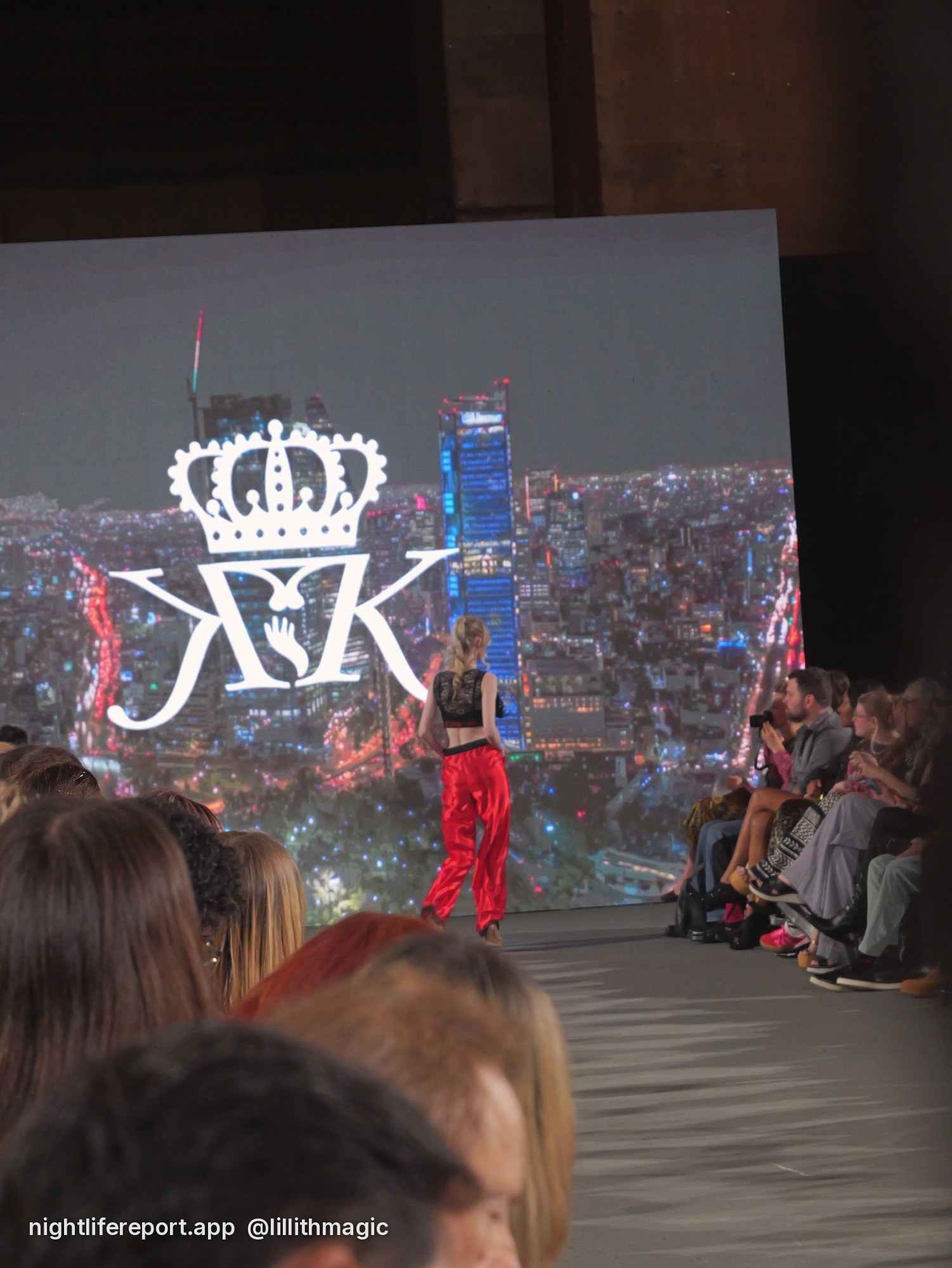 Crowd view of Ava on the Krown Kink runway, the KK crown logo on the screen behind her