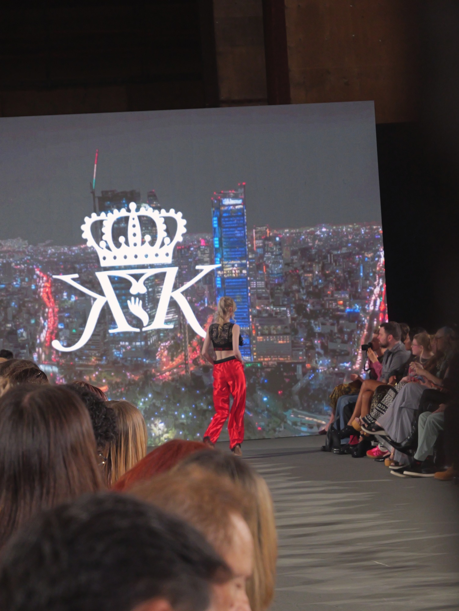 Crowd view of Ava on the Krown Kink runway, the KK crown logo on the screen behind her