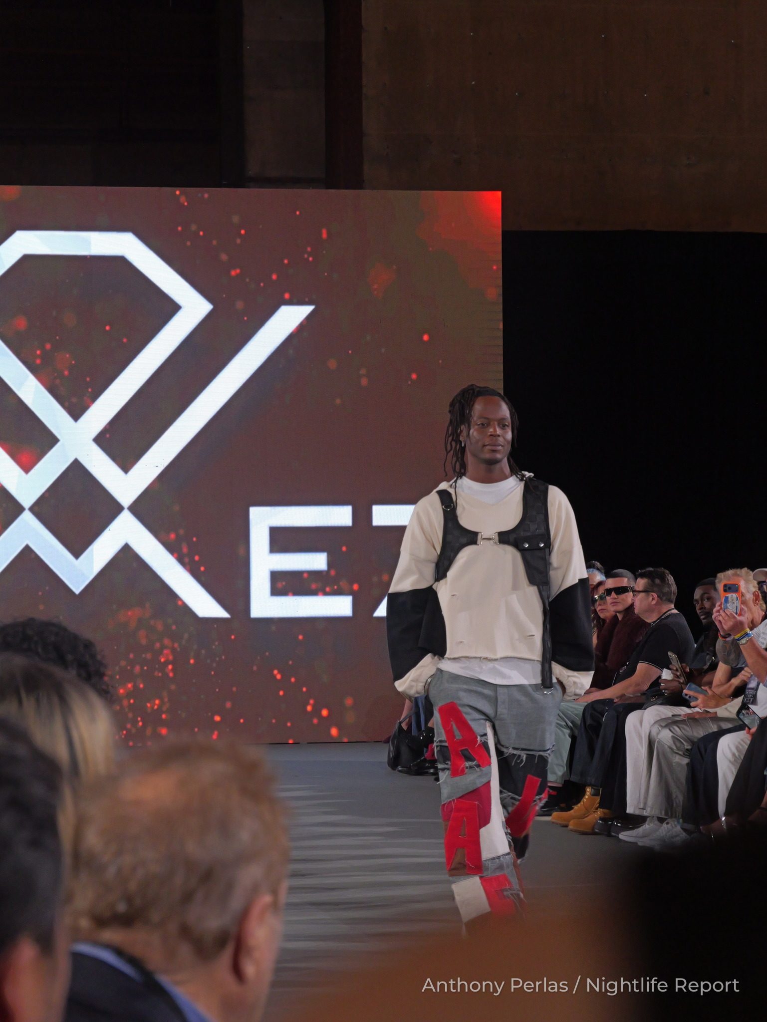 Runway look by Dimez at The Bureau Fashion Week LA, The Opening: white hoodie with a black harness and red and white cargo trousers.