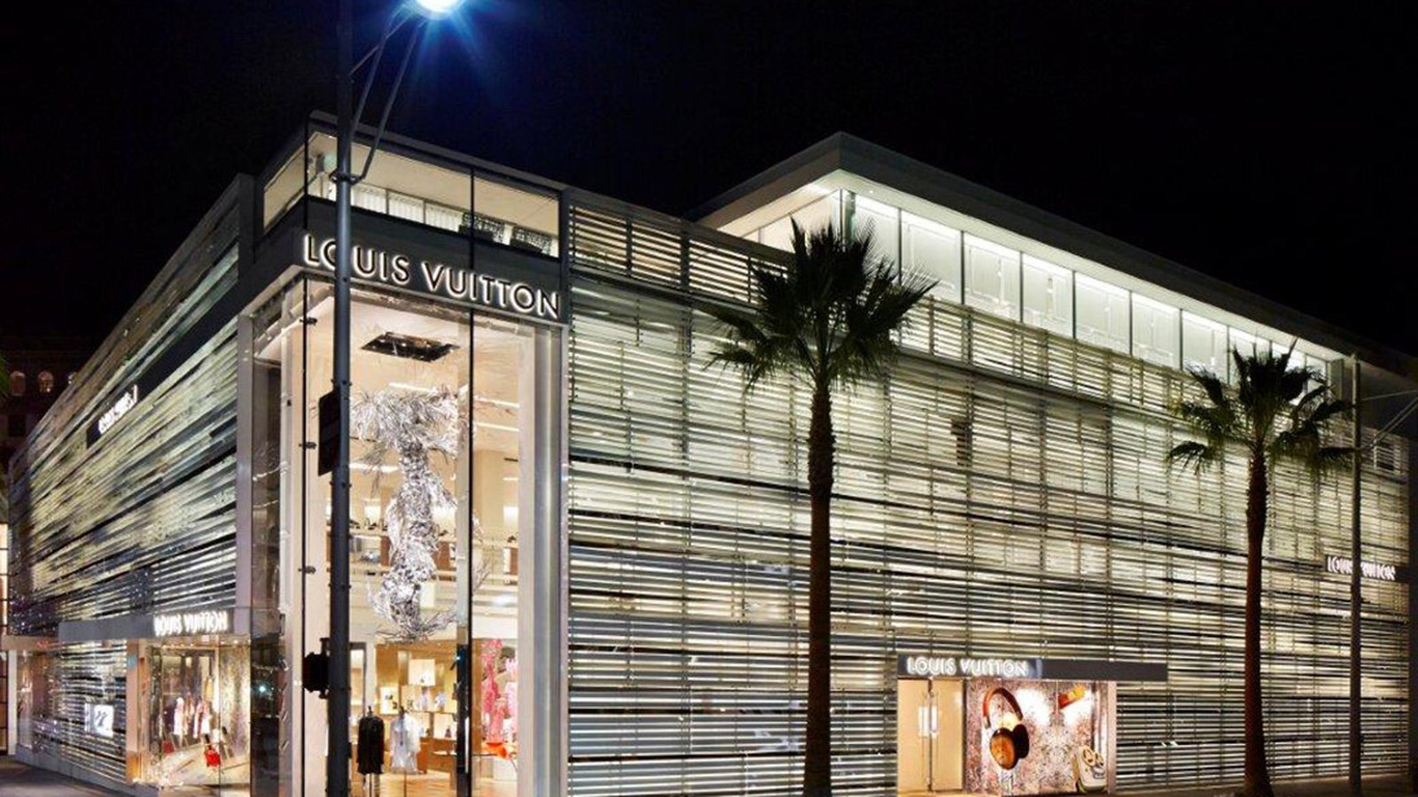 Louis Vuitton store exterior on Rodeo Drive in Beverly Hills at night, lit windows and palm trees