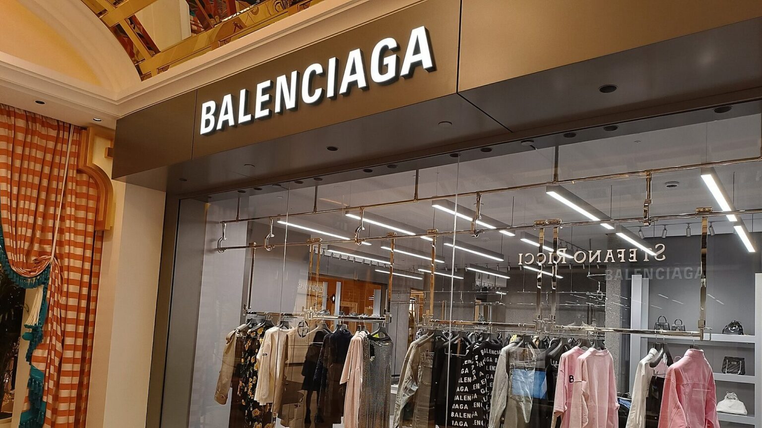 Balenciaga boutique storefront with the brand's sign above a window of clothing racks