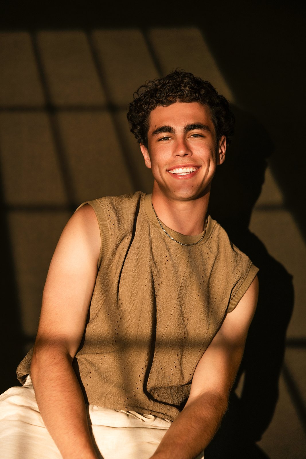 Kevin Fernandez smiling in an olive knit sleeveless top, seated in warm window light