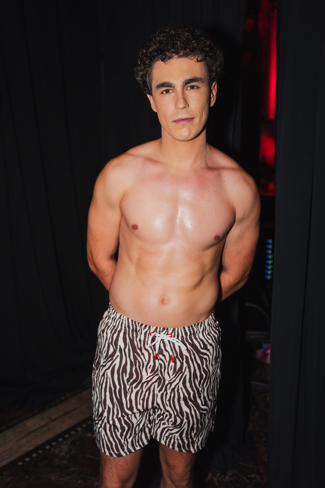 Kevin Fernandez backstage in zebra-print swim shorts against a dark curtain