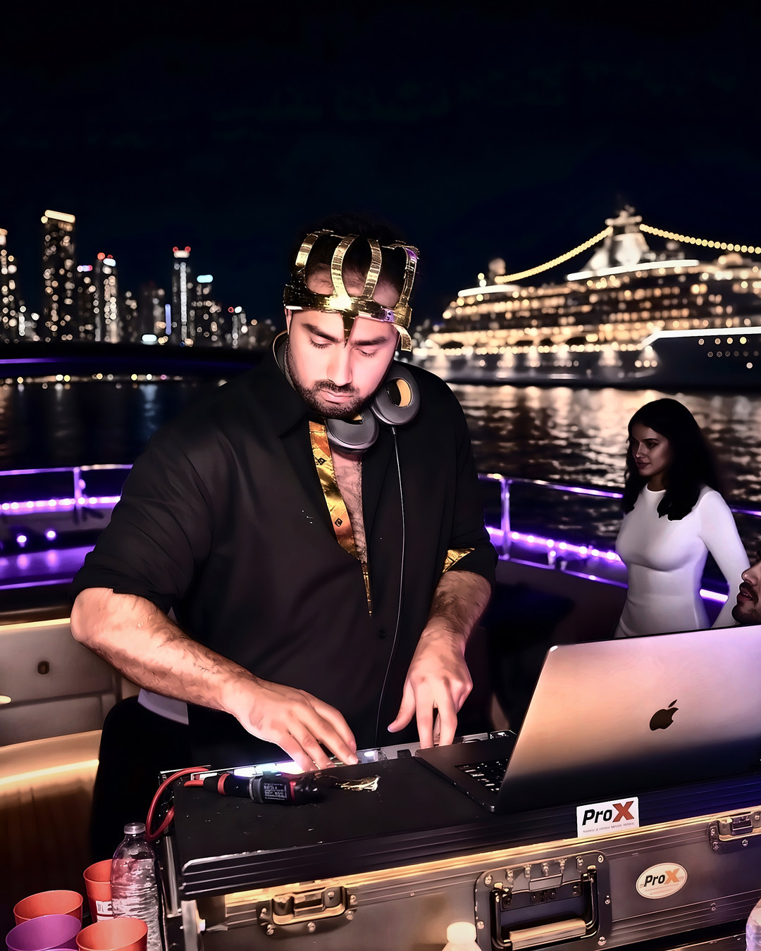 DJ in a gold crown mixing on the top deck of a yacht at night