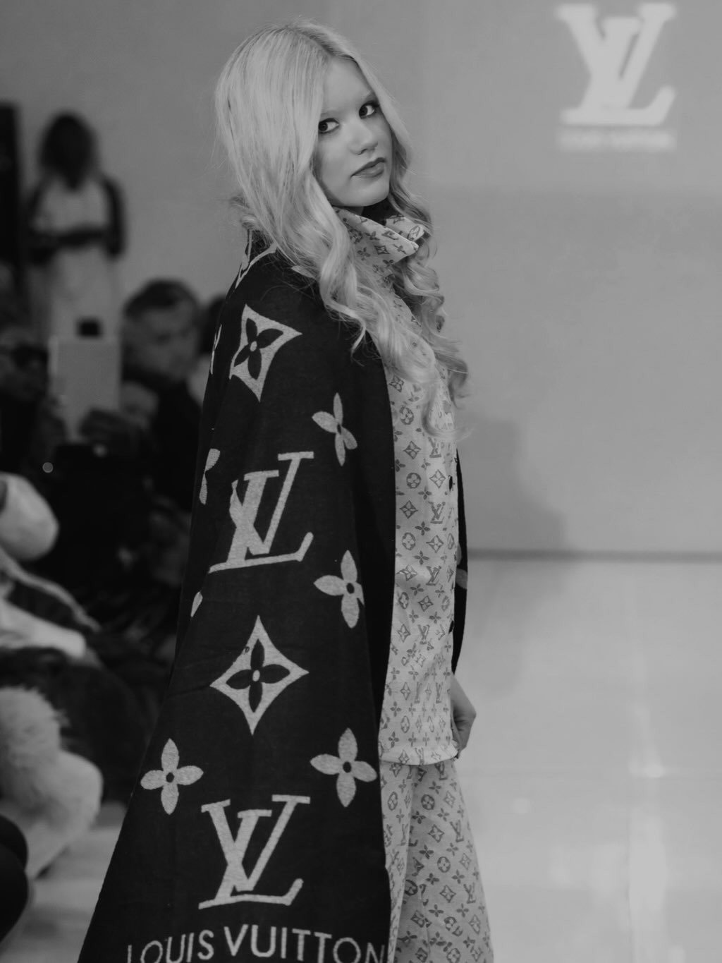 Sophie Rann on the runway in black and white, looking back over her shoulder in a monogram cape